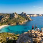 Groupe de randonneurs admirant une vue panoramique sur une plage de sable blanc, mer turquoise et falaises rocheuses en Corse du Sud.