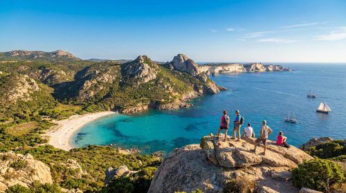 Groupe de randonneurs admirant une vue panoramique sur une plage de sable blanc, mer turquoise et falaises rocheuses en Corse du Sud.