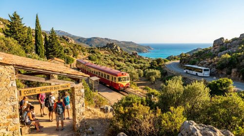 Groupe de voyageurs à un arrêt de bus/train en Corse, avec un bus sur une route côtière et un train à quai, face à la mer turquoise.