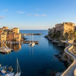 Vue aérienne du vieux port de Bastia avec ses bateaux et la citadelle historique surplombant la mer Méditerranée.