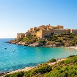 Vue panoramique de la citadelle historique de Calvi surplombant une plage de sable et une eau turquoise en Corse.