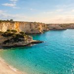 Que faire en Corse-du-Sud pour un séjour inoubliable Plage de sable fin bordée de falaises calcaires surplombant une mer turquoise en Corse sous un soleil radieux.