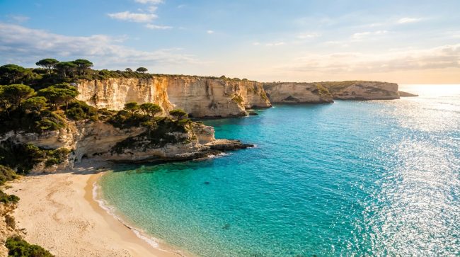 Plage de sable fin bordée de falaises calcaires surplombant une mer turquoise en Corse sous un soleil radieux.