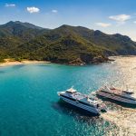 Deux ferries naviguant sur une mer turquoise le long des côtes montagneuses de la Corse.