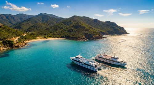 Deux ferries naviguant sur une mer turquoise le long des côtes montagneuses de la Corse.