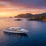 Ferry Marseille Corse : tarifs, durées et compagnies Un ferry blanc navigue sur une mer calme au coucher du soleil près des côtes rocheuses de la Corse.