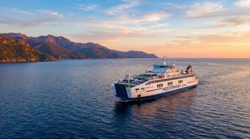 Un ferry Corsica Linea naviguant sur une mer calme devant les montagnes corses au coucher du soleil.