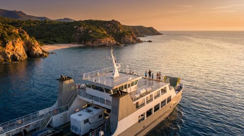 Ferry transportant des passagers et un camping-car naviguant le long des côtes rocheuses de Corse au coucher du soleil.