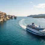 Un ferry naviguant en mer sous les falaises blanches de la ville fortifiée de Bonifacio en Corse.