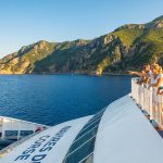 Une famille regarde la côte corse depuis le pont d'un ferry sous un ciel ensoleillé.