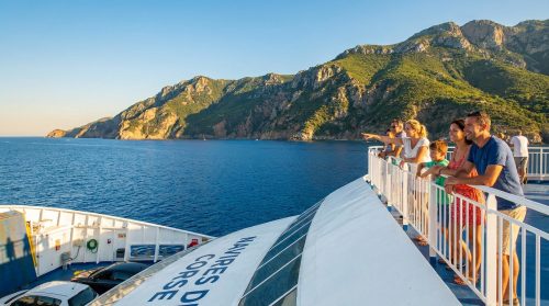 Une famille regarde la côte corse depuis le pont d'un ferry sous un ciel ensoleillé.