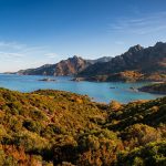 Vue panoramique d'une baie en Corse avec des montagnes aux couleurs d'automne dominant une mer turquoise.