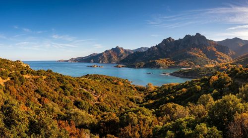 Vue panoramique d'une baie en Corse avec des montagnes aux couleurs d'automne dominant une mer turquoise.